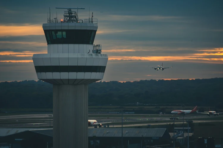 Airport air traffic control tower at sunset with aircraft on final approach