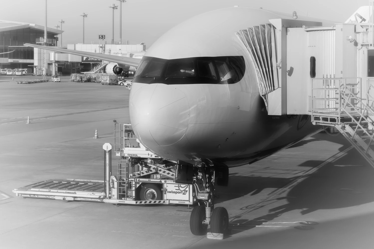 Black-and-white view of a widebody airliner parked at the gate with a jet bridge and loader in place — aircraft finance and repossession in Ukraine
