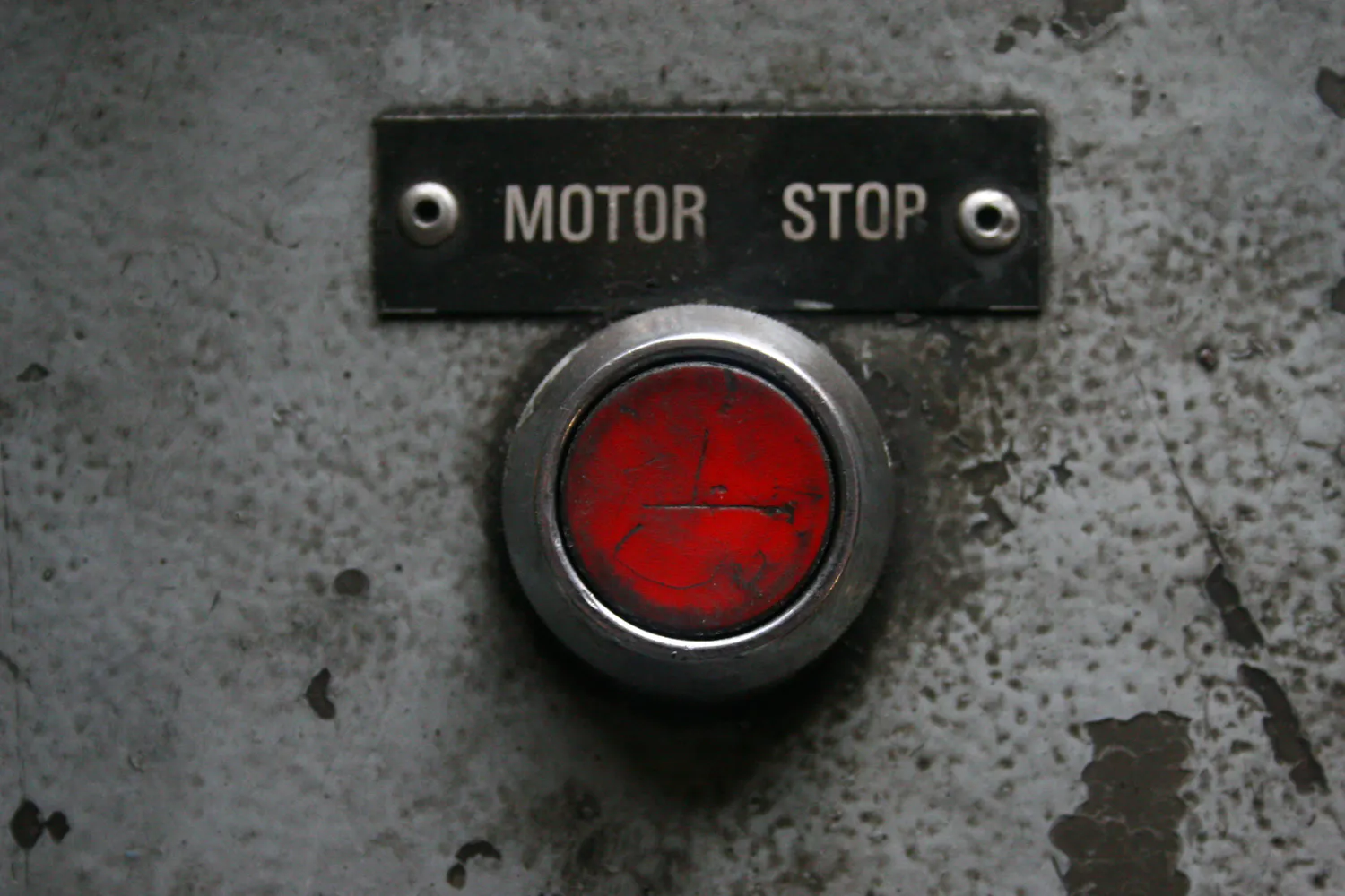 A worn red push button under a metal plate reading Motor Stop